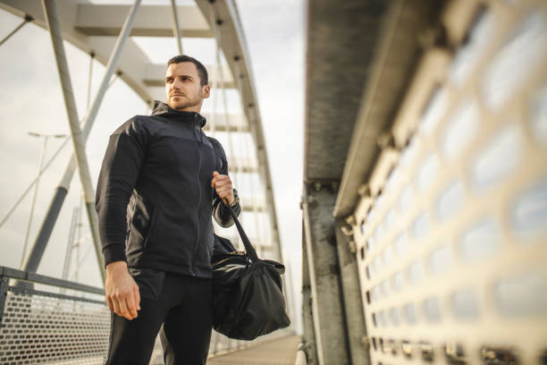 sporty man walking to home with bag on his shoulder after workout outdoors